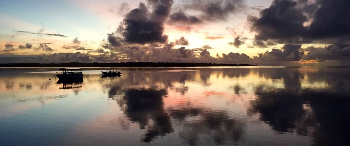 A calm lake at sunset with a boat in the foreground and a silhouette of trees on the horizon.