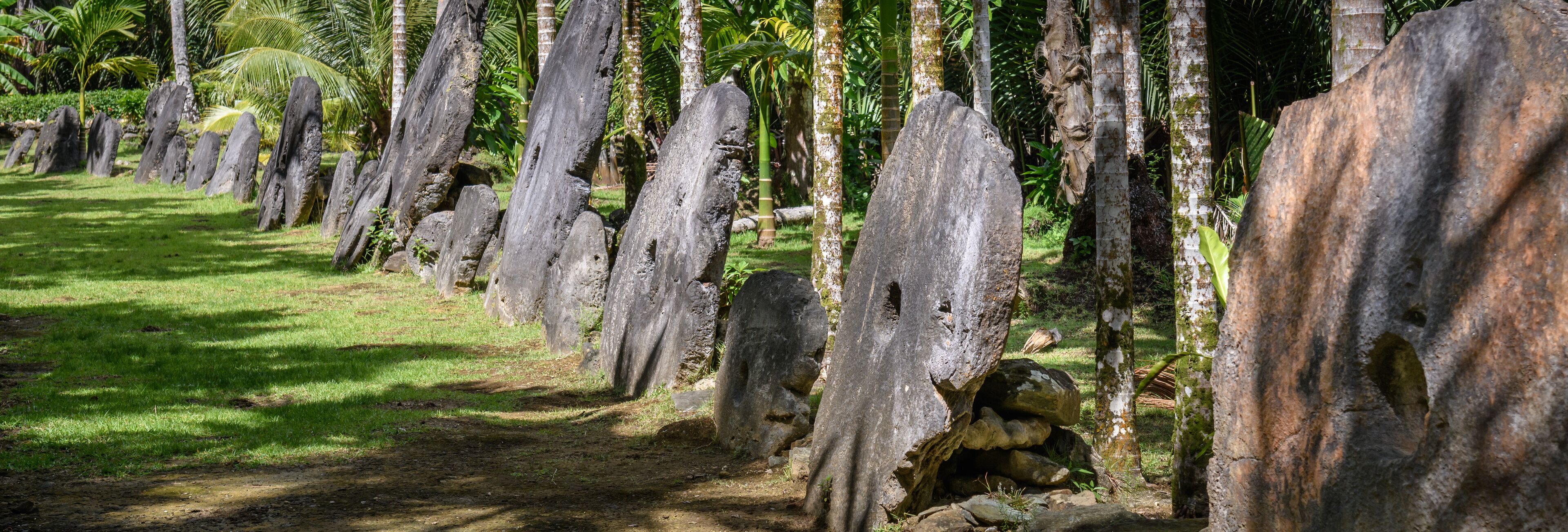 A pathway lined with tall, weathered stone pillars in a lush, green landscape.