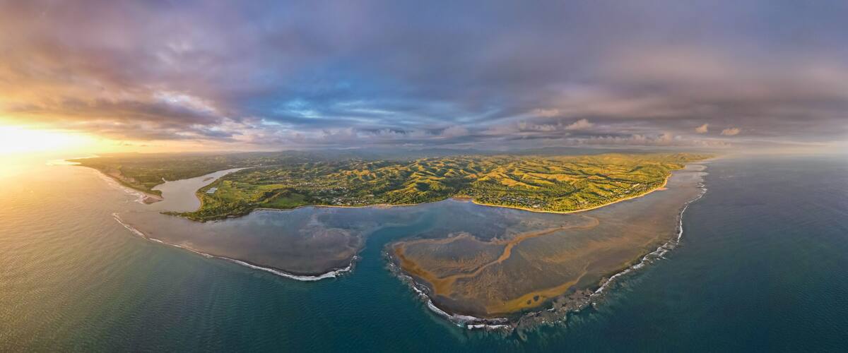 An aerial view of a coastal landscape with a river, green hills, and a large body of water.