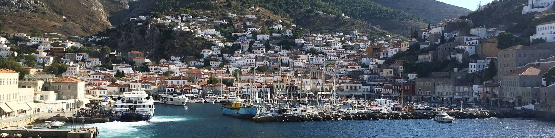 A coastal town with a harbor filled with boats, surrounded by hills and white buildings.
