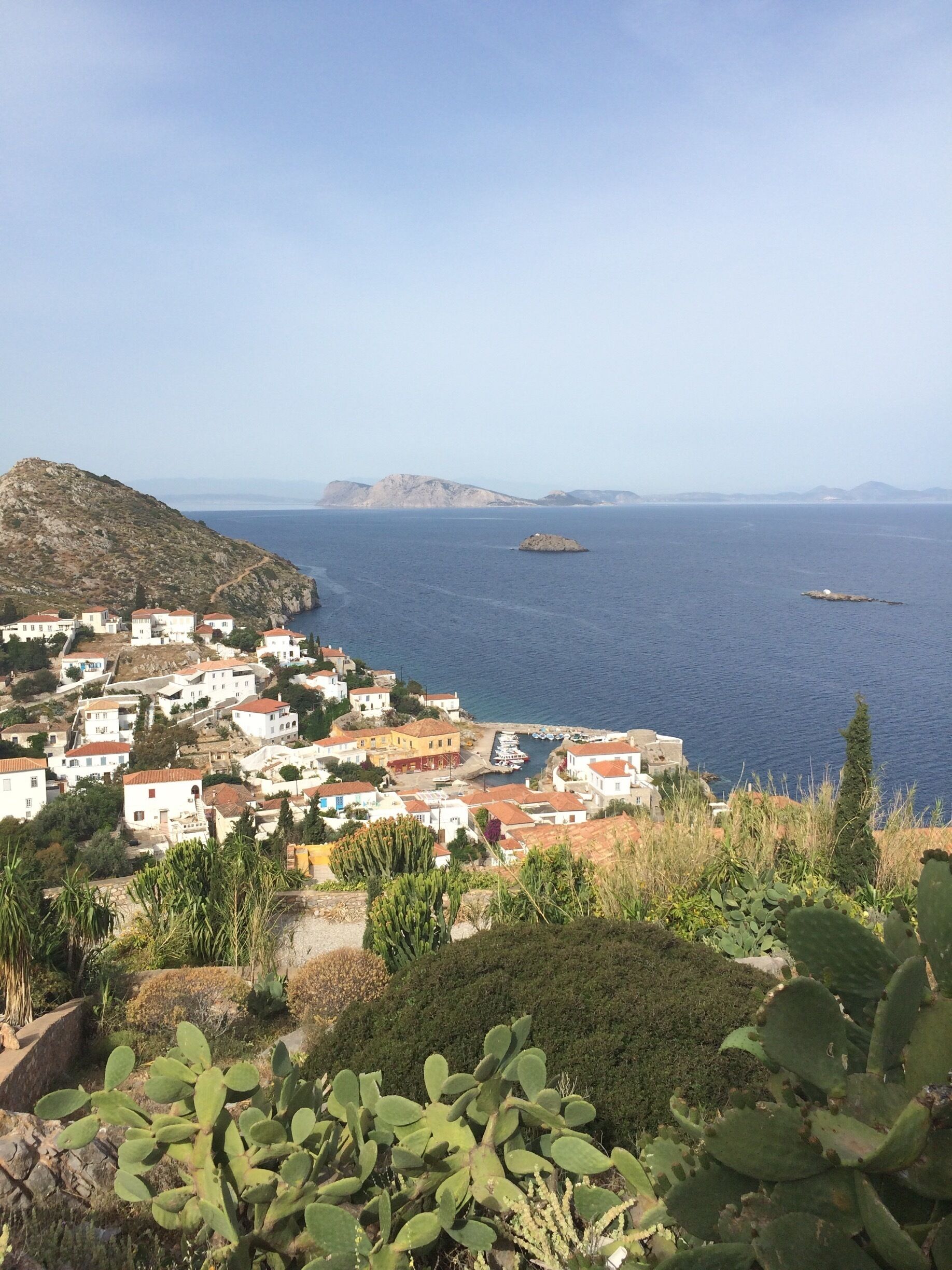 A coastal village with white buildings and red roofs, surrounded by mountains and the sea.