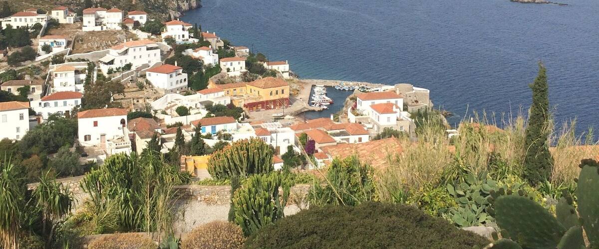 A coastal village with white buildings and red roofs, surrounded by mountains and the sea.