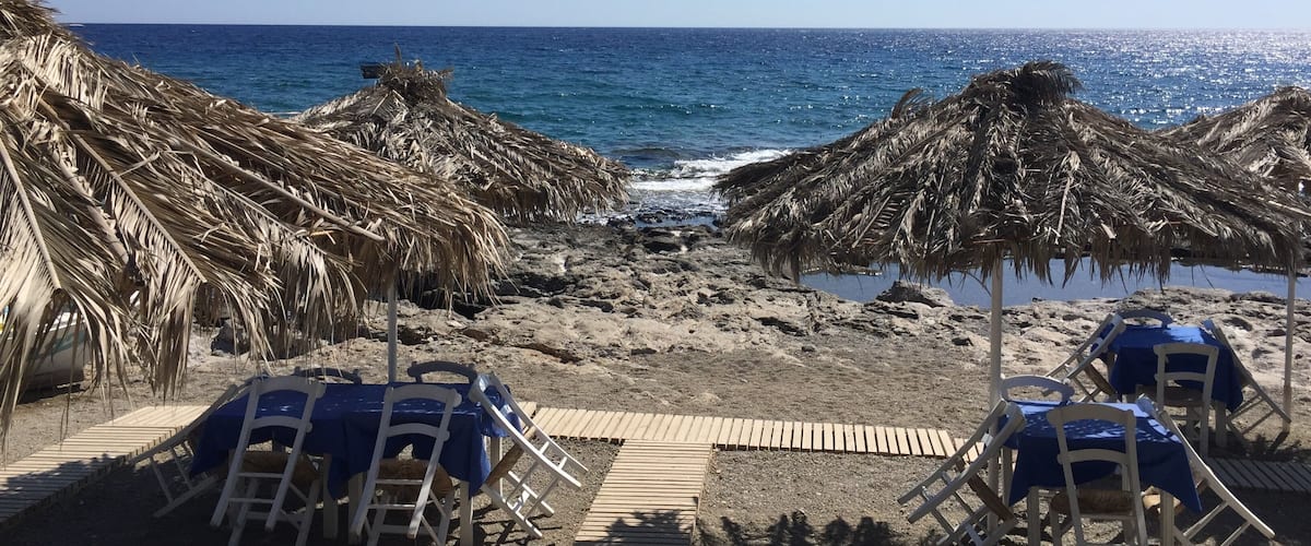 A beach with thatched umbrellas and lounge chairs.