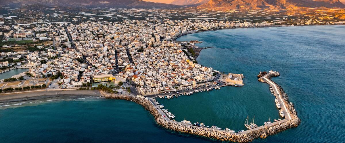 An aerial view of a coastal city with a prominent harbor, surrounded by mountains.
