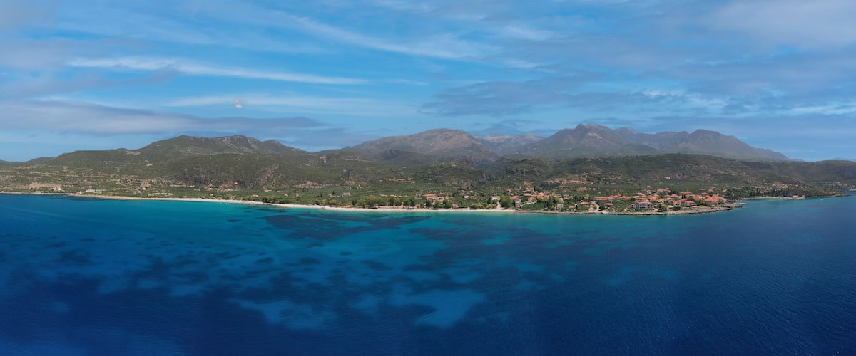 A coastal town with a mountain range in the background and clear blue waters.