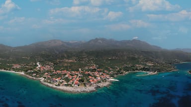 Vista aérea de un pueblo costero con montañas al fondo, aguas turquesas cristalinas y una pequeña isla cerca.