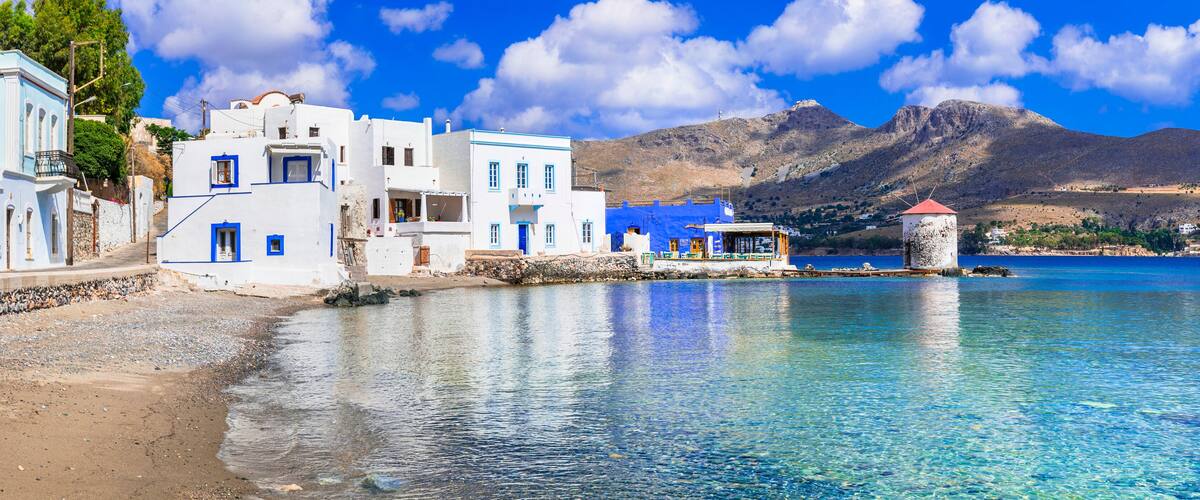 A coastal village with white buildings, a clear blue sea, and mountains in the background.