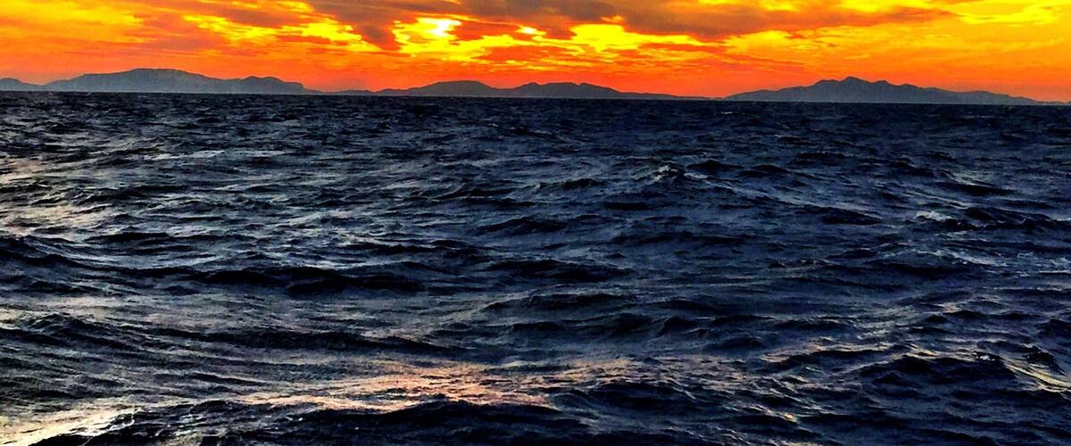 A sunset over the ocean with waves and distant mountains.