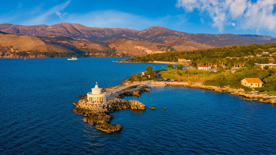 A coastal landscape with a white lighthouse, rocky shoreline, and a boat on the water.