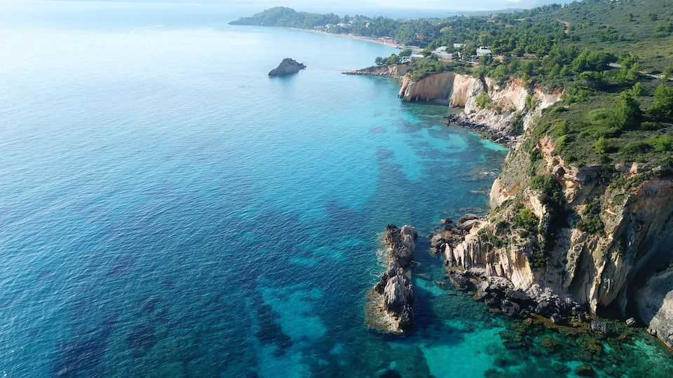 A coastal landscape with clear turquoise waters, rocky cliffs, and a distant view of a town.