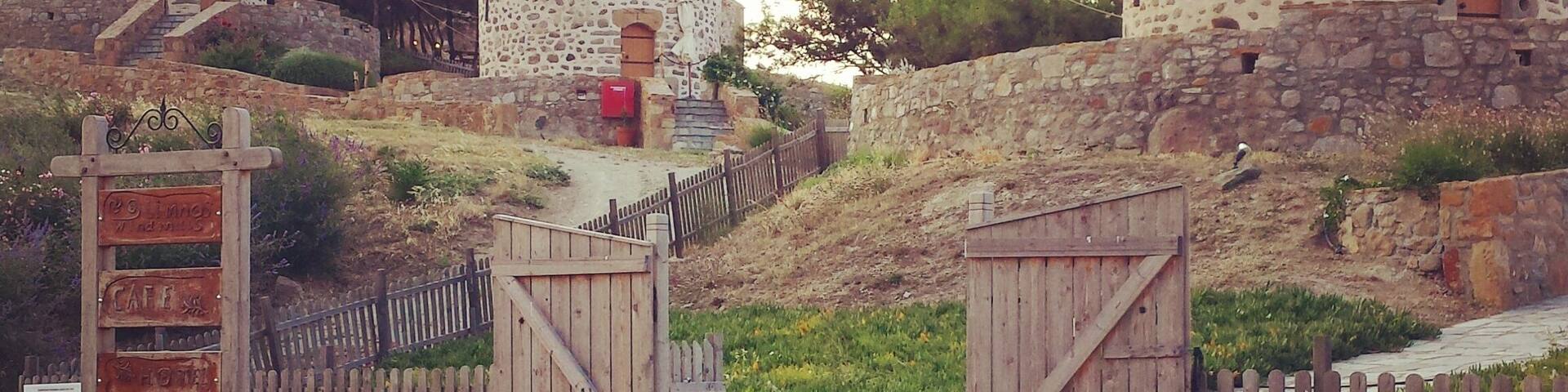 Traditional windmills with stone walls, wooden gates, and a signboard.