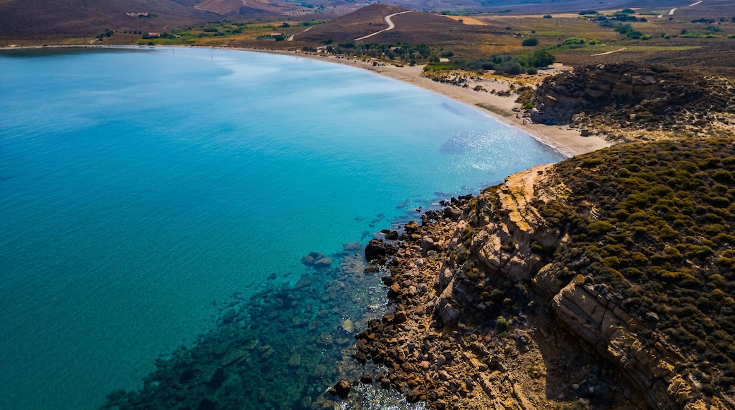 High-angle aerial view of the Neftina Beach on Limnos Island, Greece, showing crystal clear turquoise waters meeting a sandy shoreline backed by rugged, arid Mediterranean hills.