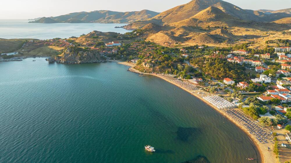 A coastal town with a beach, houses, and mountains in the background.