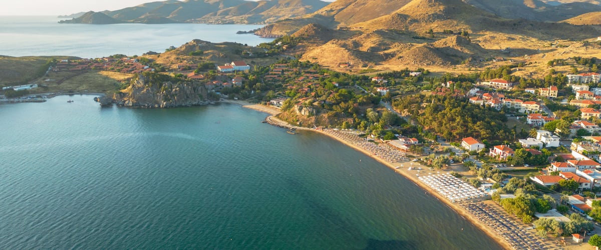 A coastal town with a beach, houses, and mountains in the background.