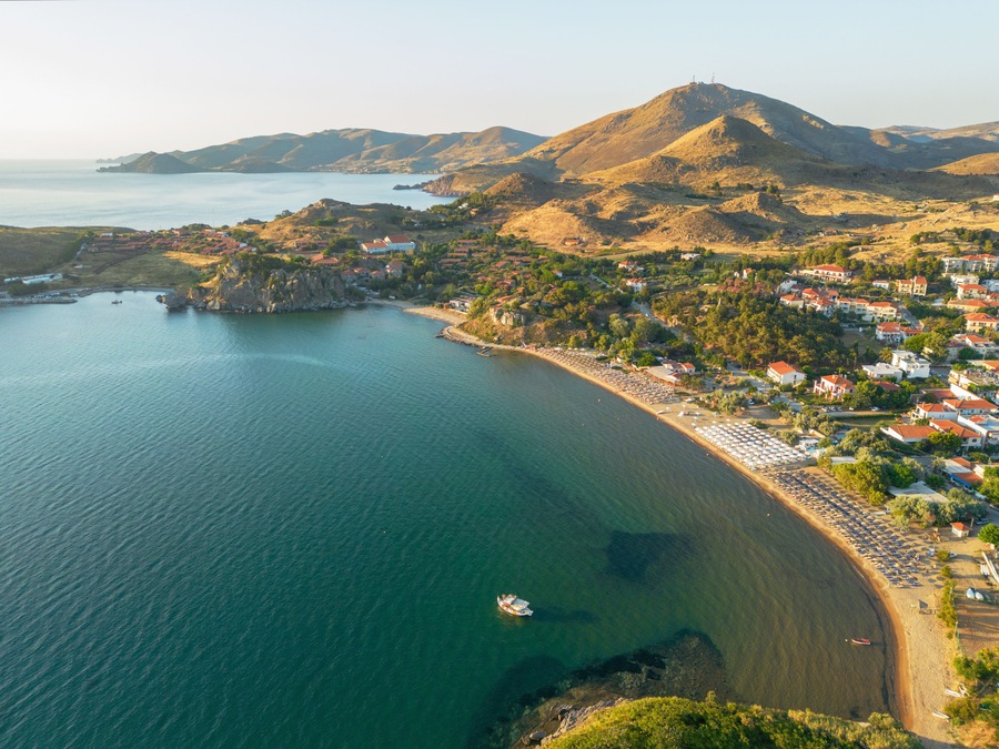 A coastal town with a beach, houses, and mountains in the background.
