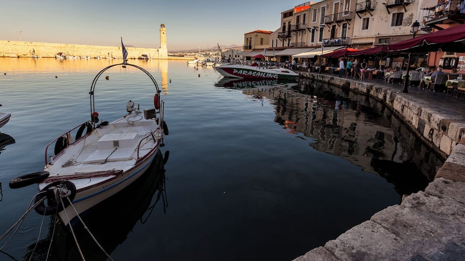 A calm harbor with boats, a lighthouse, and buildings along the waterfront.