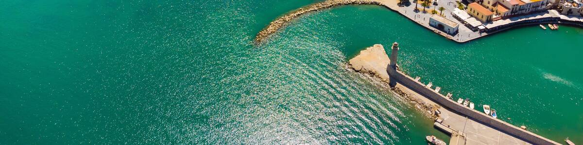 Un paysage urbain côtier avec une plage bien visible, une mer bleue et limpide, et un port fortifié.