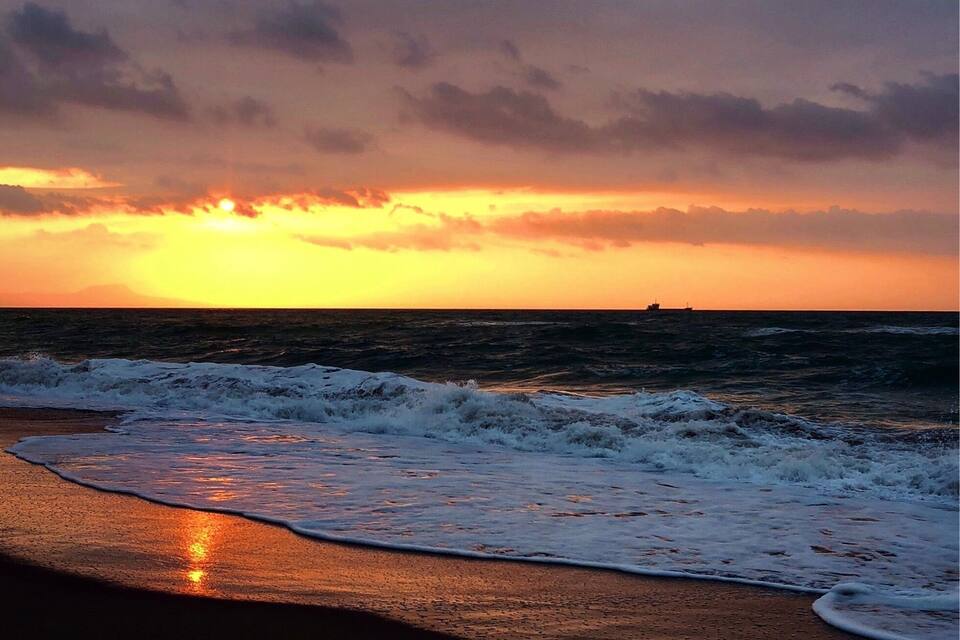 Une plage au coucher du soleil, avec des vagues qui déferlent sur le rivage et un navire à l’horizon.