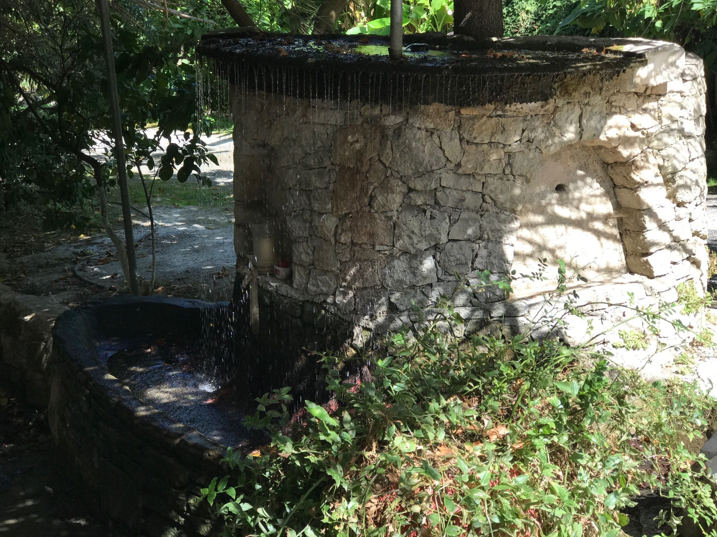 A stone water feature with a cascading water flow, surrounded by greenery and trees.