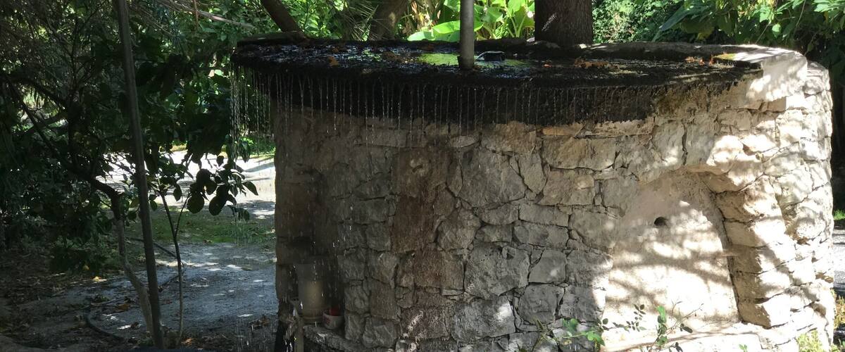 A stone water feature with a cascading water flow, surrounded by greenery and trees.