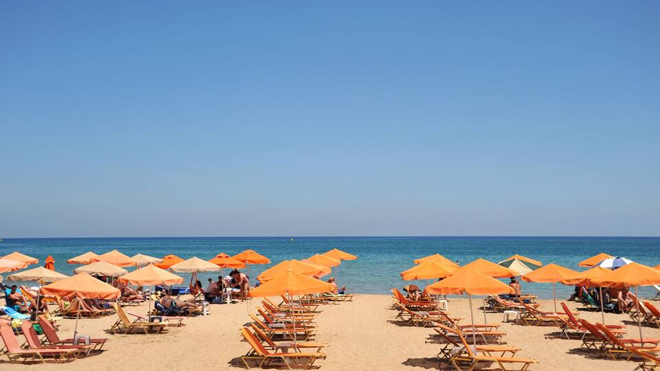 A beach with rows of orange umbrellas and sun loungers.