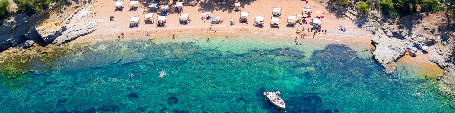 An aerial view of a beach with clear turquoise waters, a small boat anchored near the shore, and several beach huts and tents.