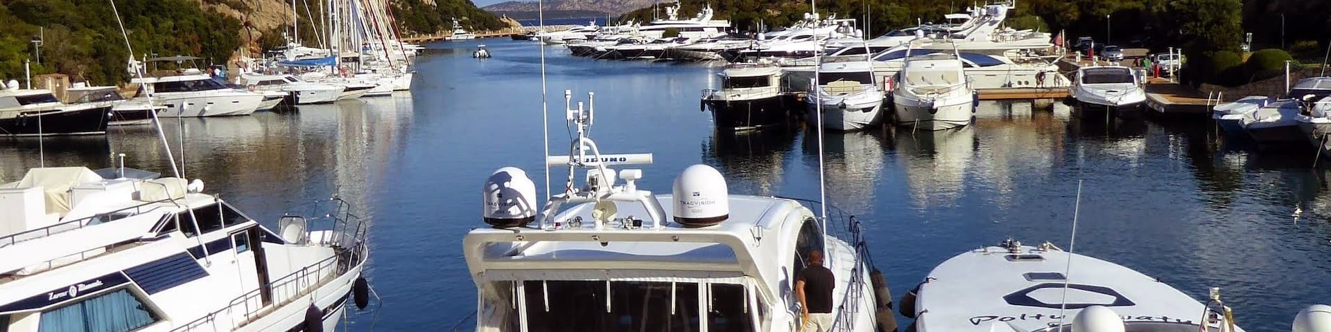 A marina with multiple yachts docked, surrounded by hills and clear skies.