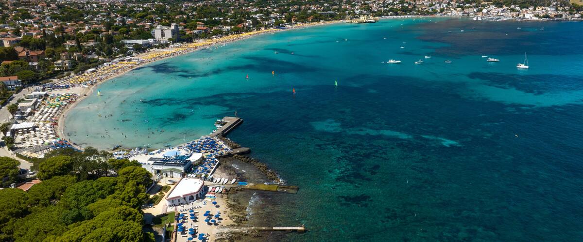 A coastal town with a beach, clear turquoise waters, and a rocky shoreline.
