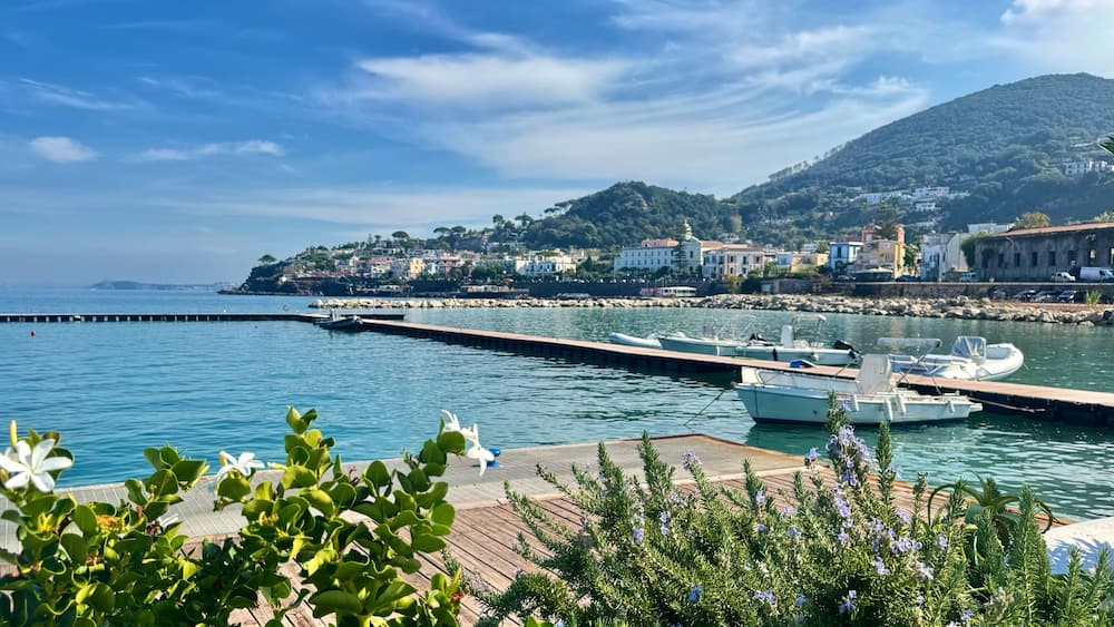 A coastal town with a pier, boats, and a mountainous backdrop.
