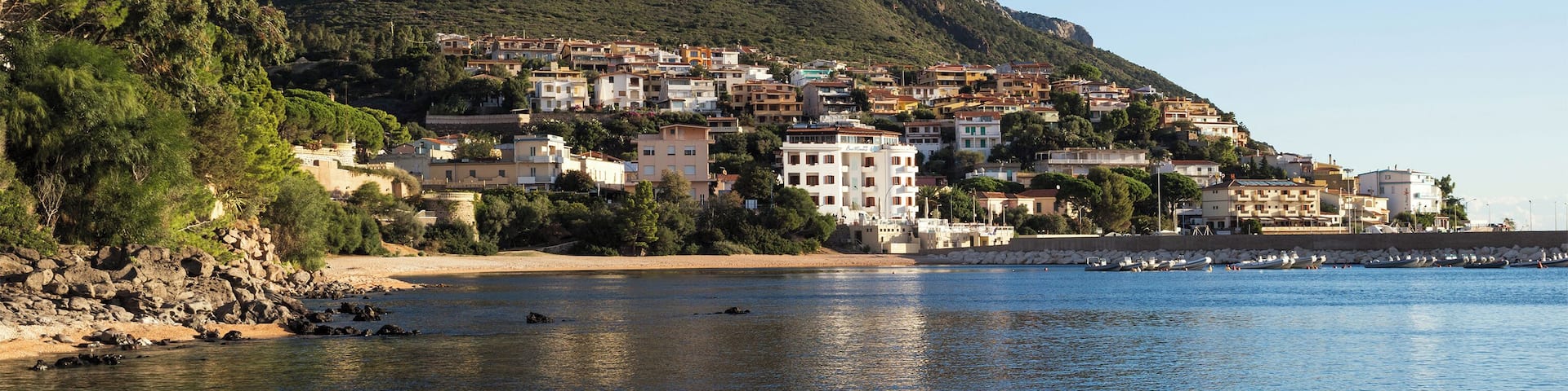 A coastal town with buildings on a hillside, a beach, and a rocky shoreline.