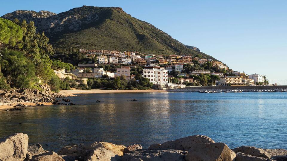 A coastal town with buildings on a hillside, a beach, and a rocky shoreline.