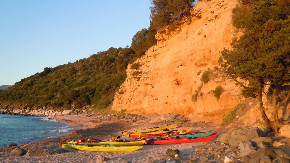 A rocky beach with kayaks and a cliff.