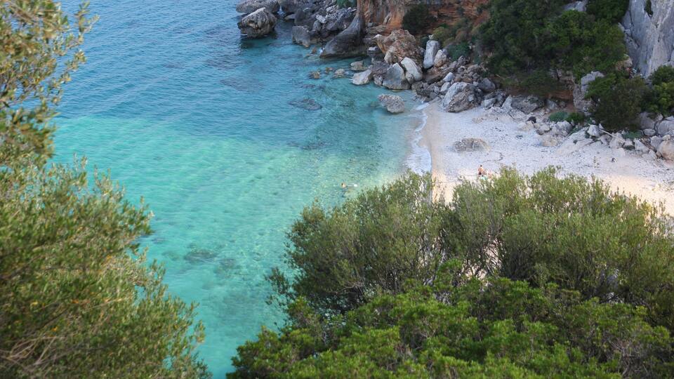 A coastal landscape with clear turquoise waters, rocky cliffs, and dense greenery.