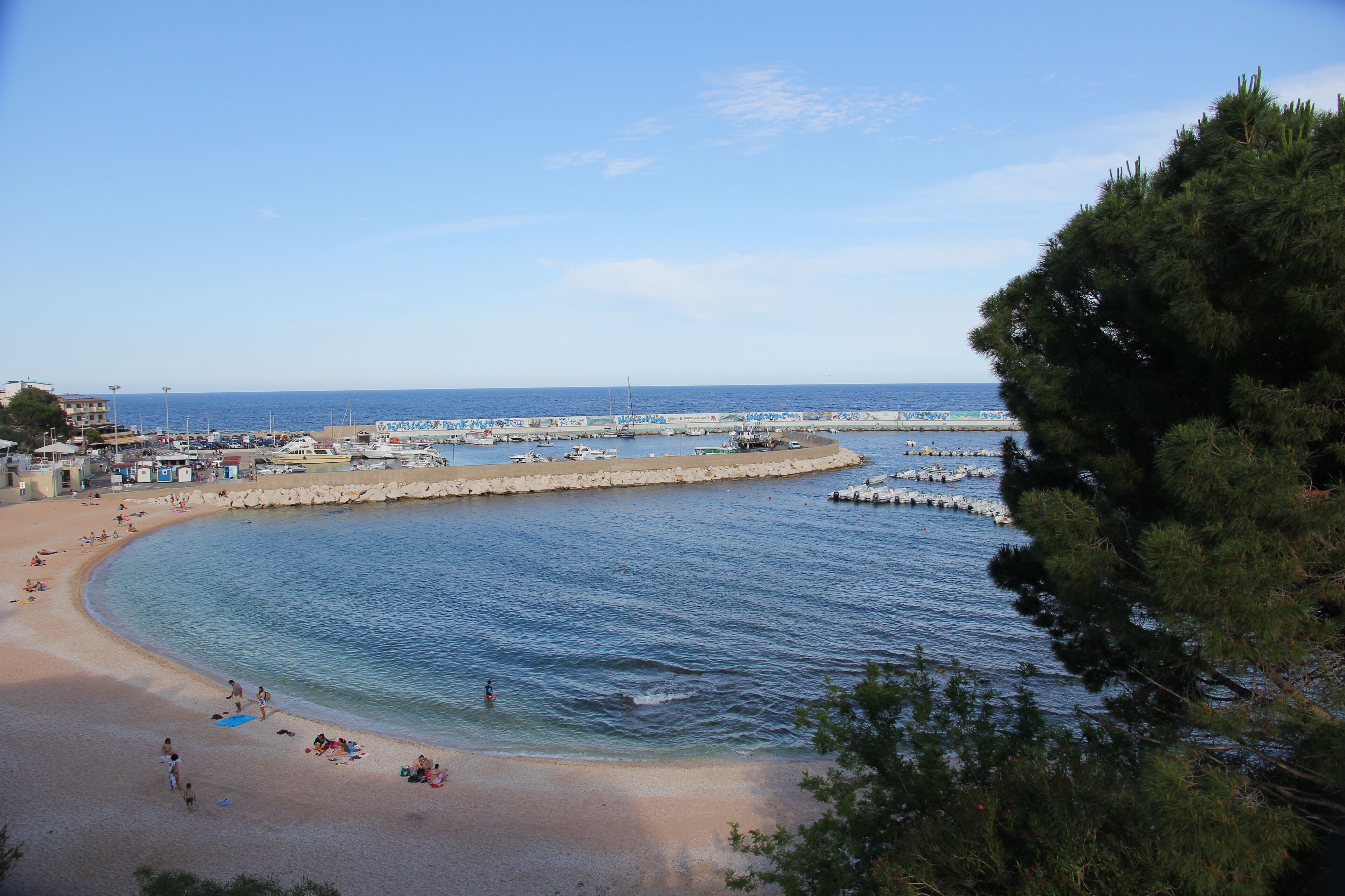 A coastal beach with clear waters, a sandy shore, and a pier extending into the sea.