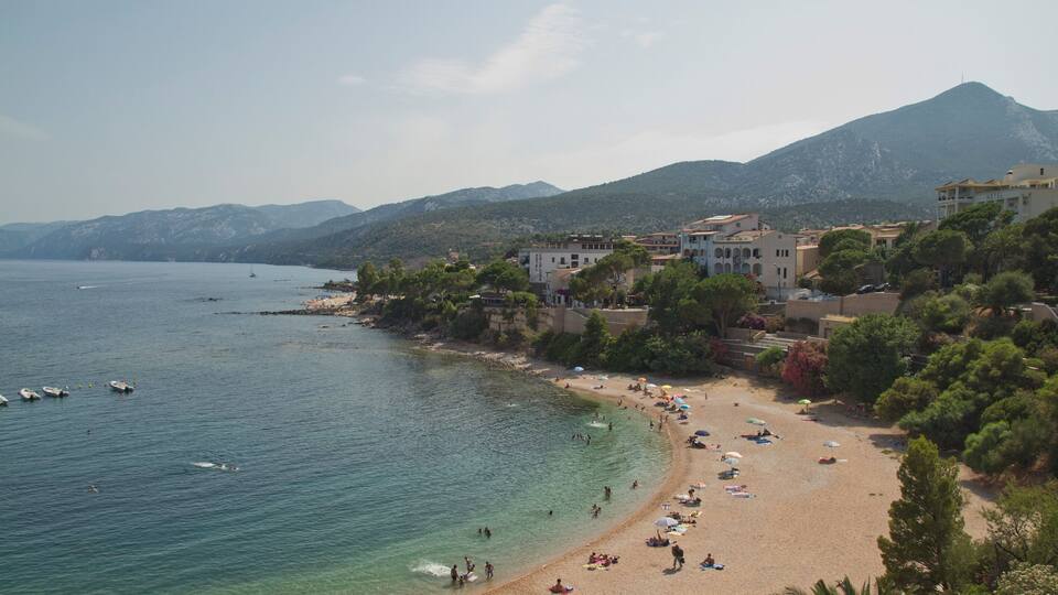 A coastal town with a beach, boats, and mountains in the background.