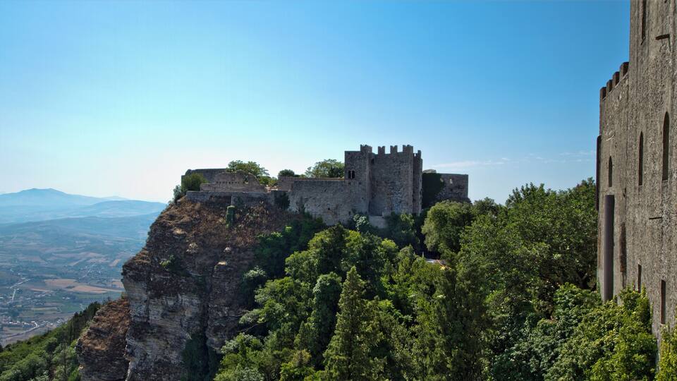 A medieval castle perched on a cliff overlooking a valley.