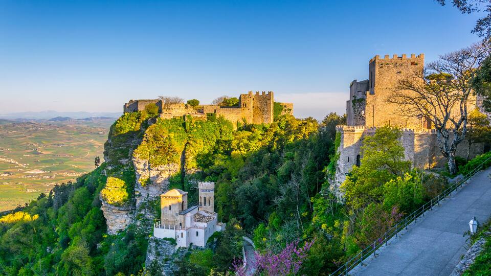 A historic castle on a hill, surrounded by lush greenery and a clear sky.