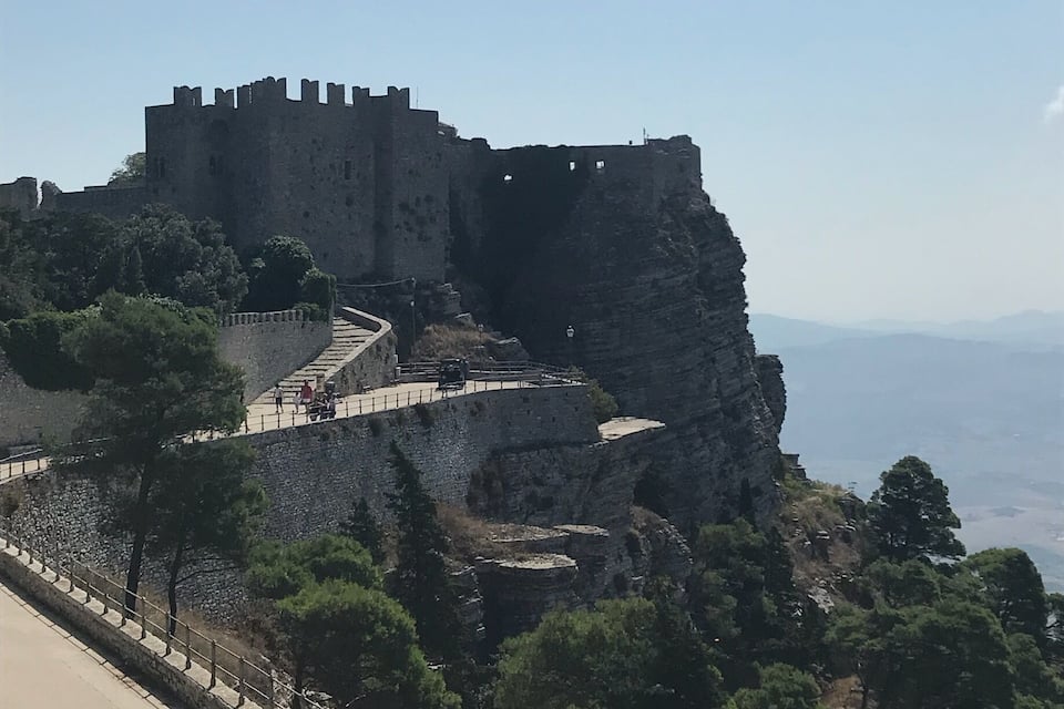 A historic castle on a hill with a paved walkway and a clear sky.