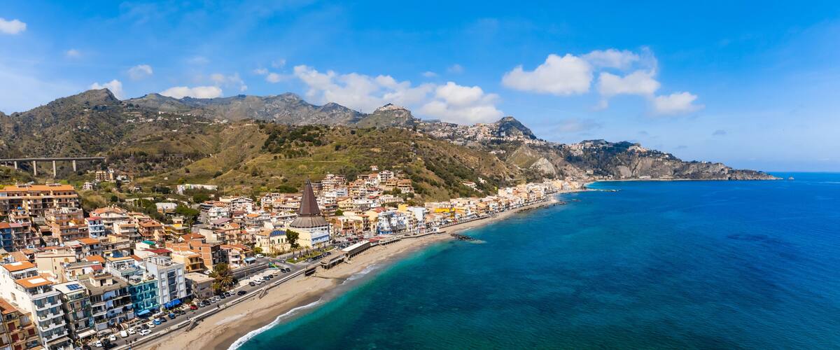 Un pueblo costero con una playa, una iglesia destacada y una cadena montañosa al fondo.