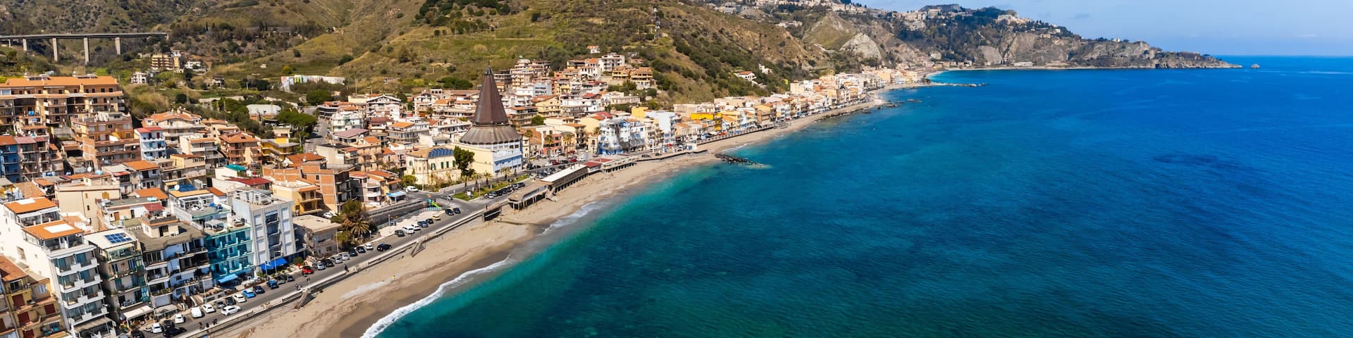 A coastal town with a beach, a prominent church, and a mountain range in the background.