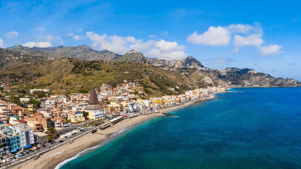 A coastal town with a beach, a prominent church, and a mountain range in the background.