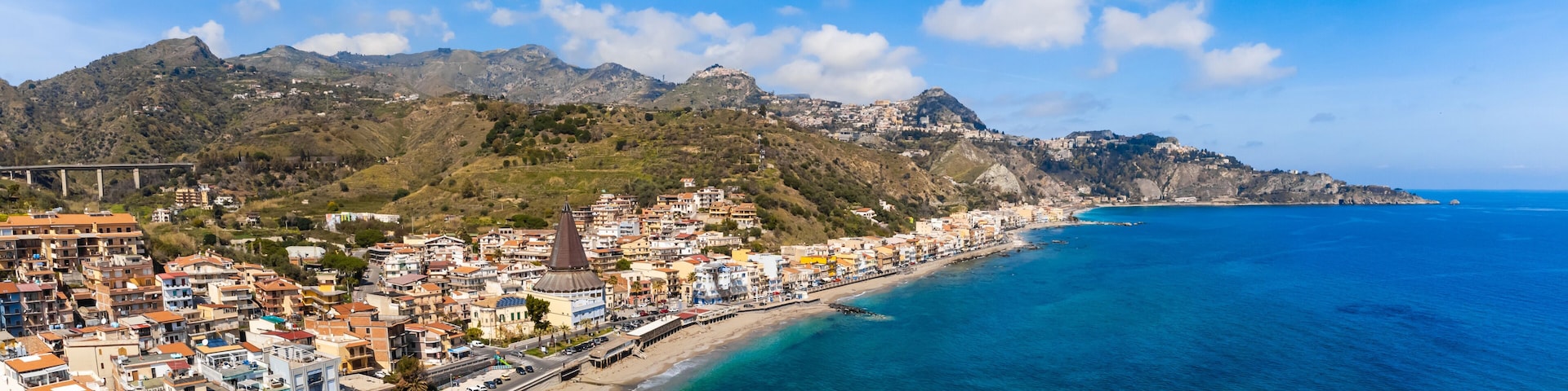 Un pueblo costero con una playa, una iglesia destacada y una cadena montañosa al fondo.