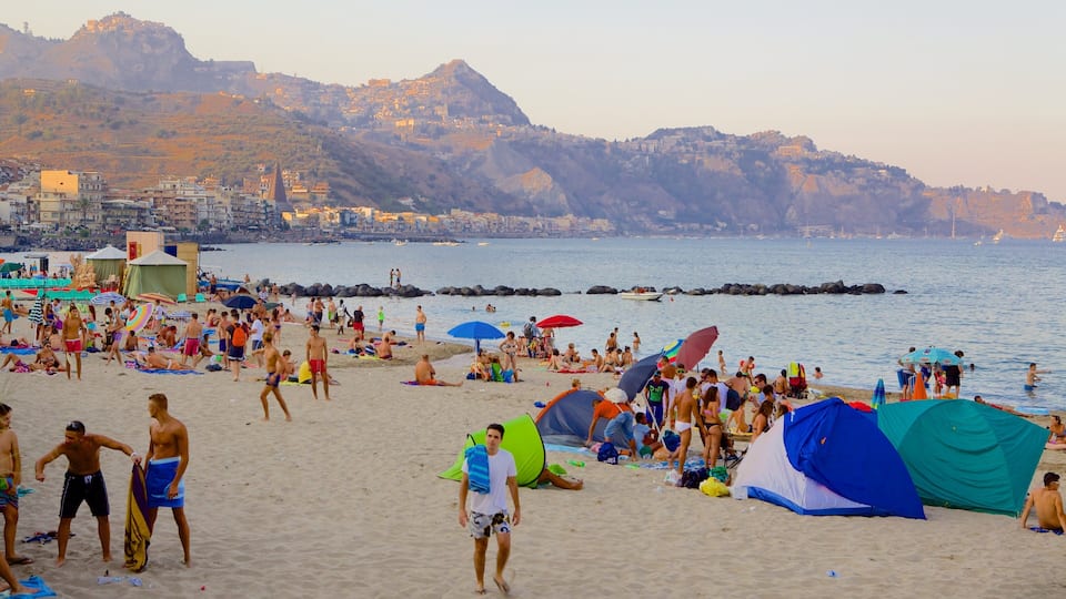 A crowded beach with tents and umbrellas, rocky coastline, and buildings in the background.