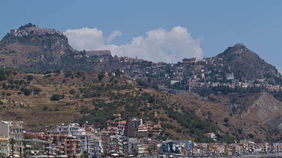 A coastal town with buildings on a hillside and a clear blue sky.