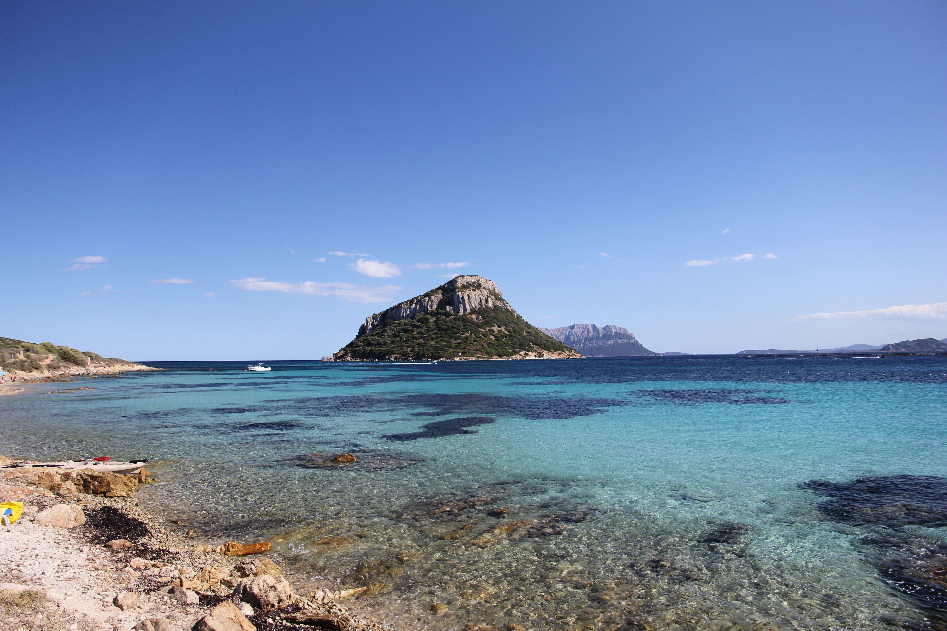 A clear blue sea with a rocky shore and a small island in the distance.