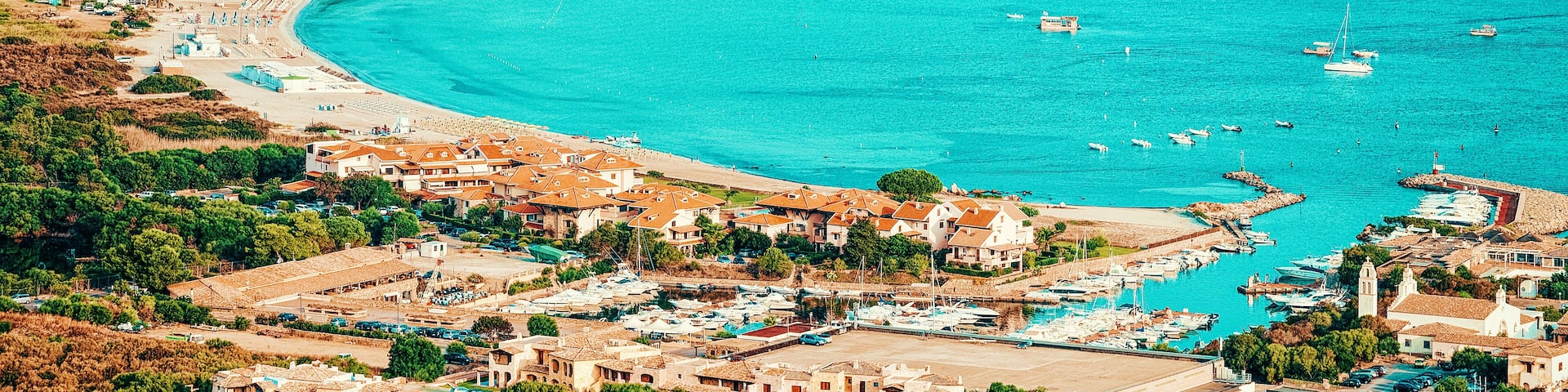 A coastal town with a turquoise bay, marina, and residential buildings.