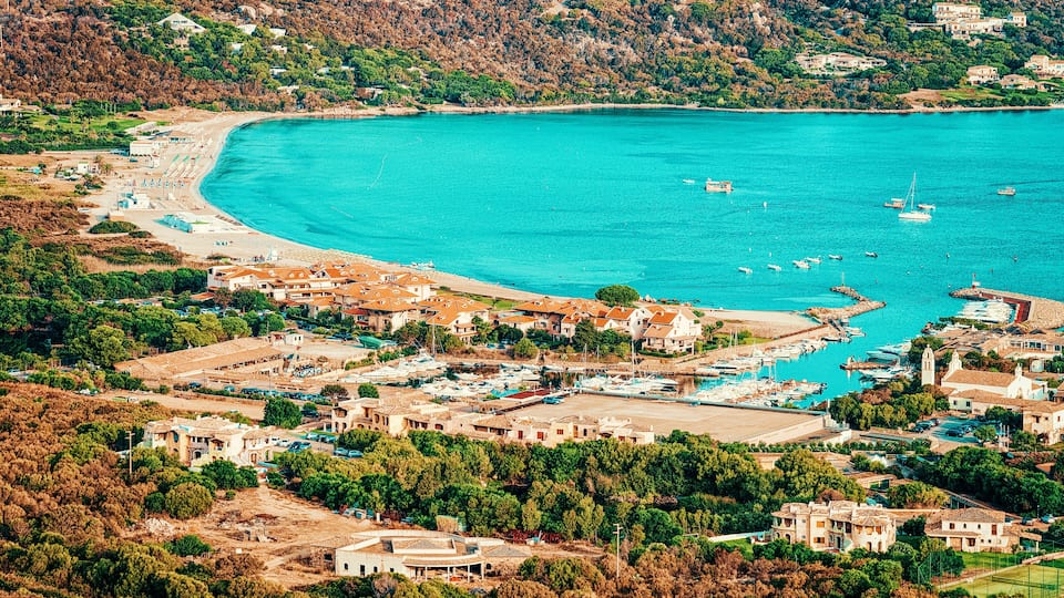 A coastal town with a turquoise bay, marina, and residential buildings.
