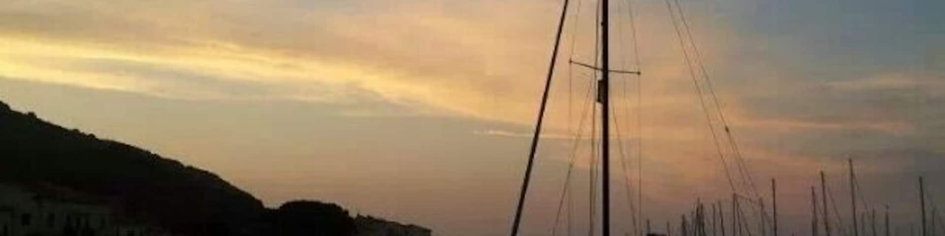 Un velero en aguas tranquilas durante el atardecer, con colinas y un cielo despejado al fondo.