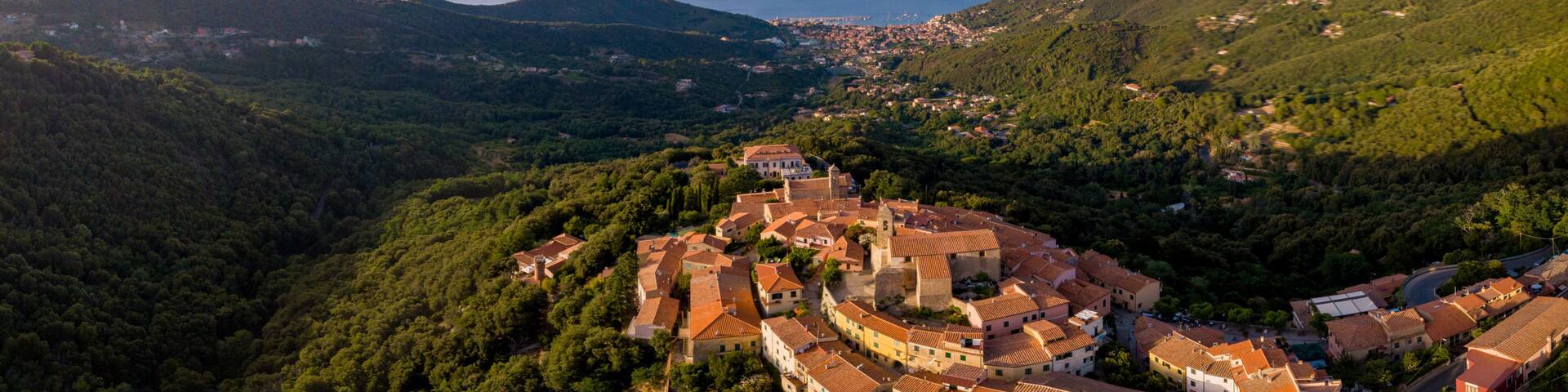 Aerial Drone Panorama of mountain old town Marciana on the islands of Elba Italy with green trees and the mediterranean sea ocean in the background