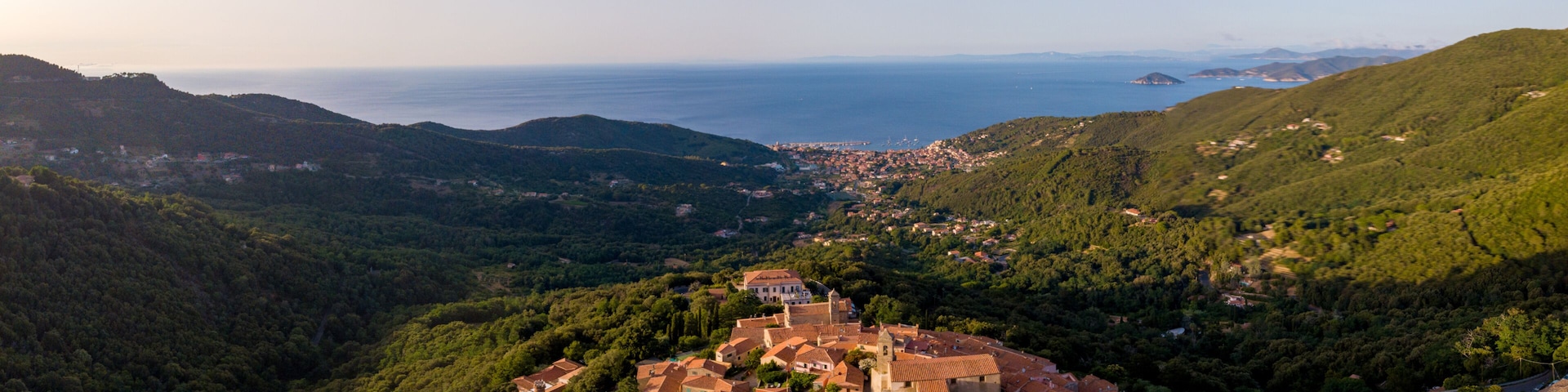 Aerial Drone Panorama of mountain old town Marciana on the islands of Elba Italy with green trees and the mediterranean sea ocean in the background